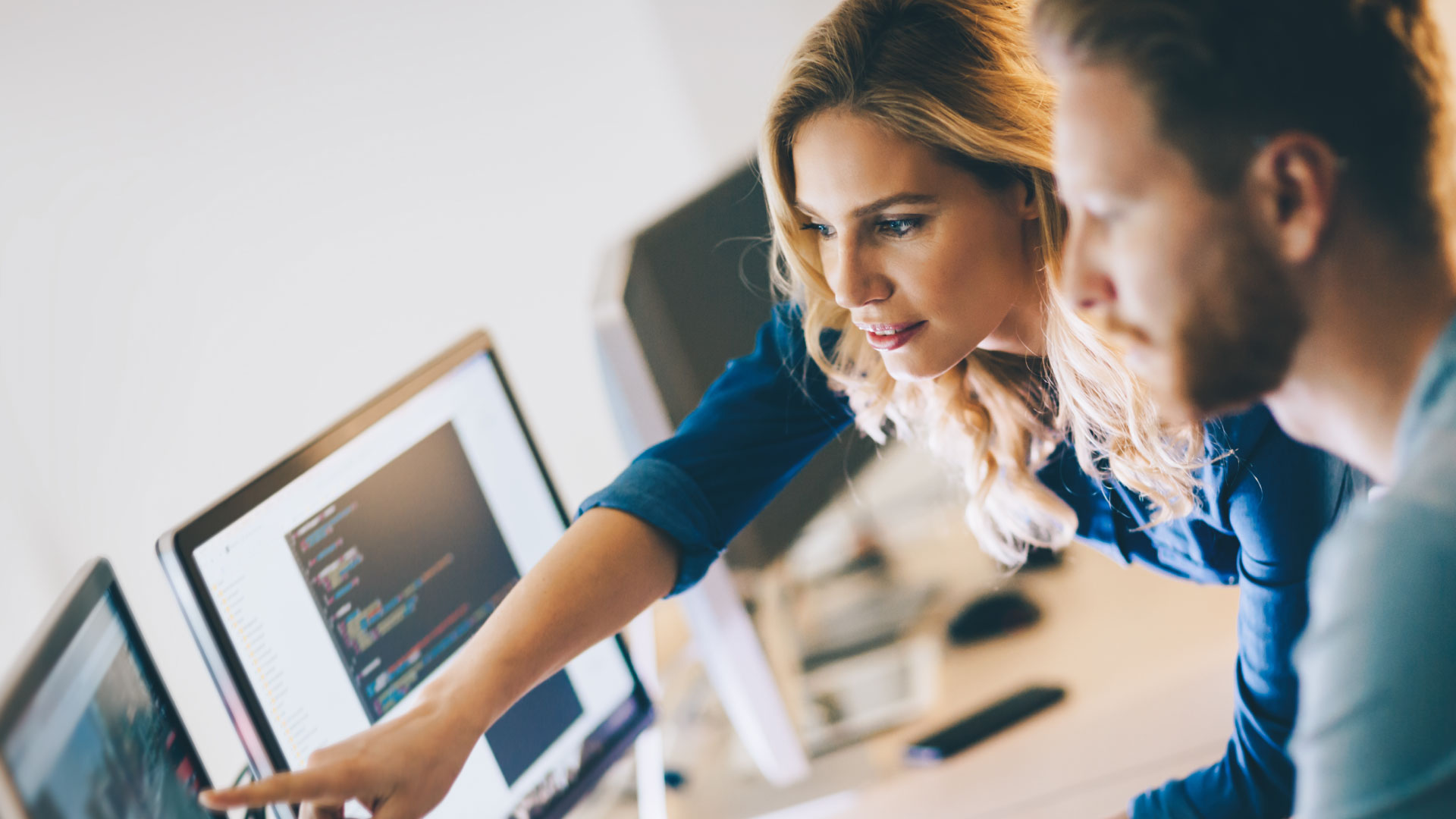 A man and a woman are looking at a screen, and the woman is pointing at it.