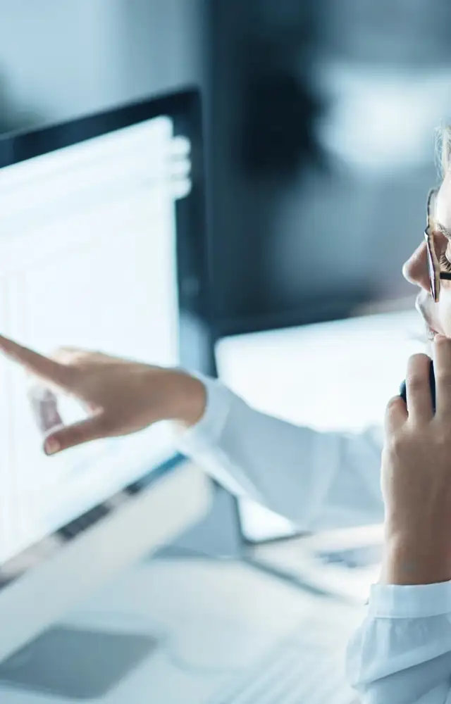 Woman pointing to a computer screen with numbers while on the phone
