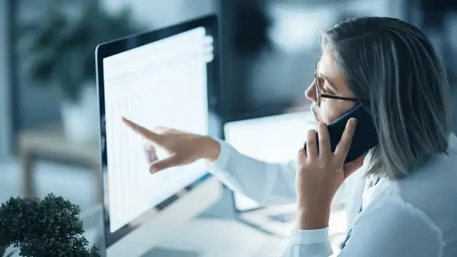 Woman pointing to a computer screen with numbers while on the phone