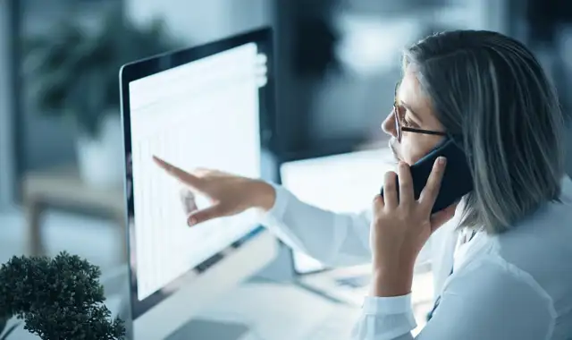 Woman speaking two someone on the phone while looking at numbers on a screen
