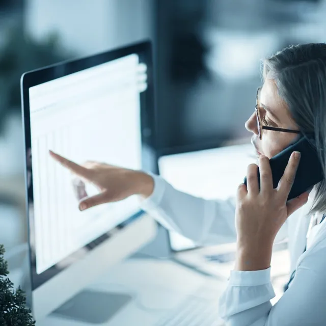Woman speaking two someone on the phone while looking at numbers on a screen