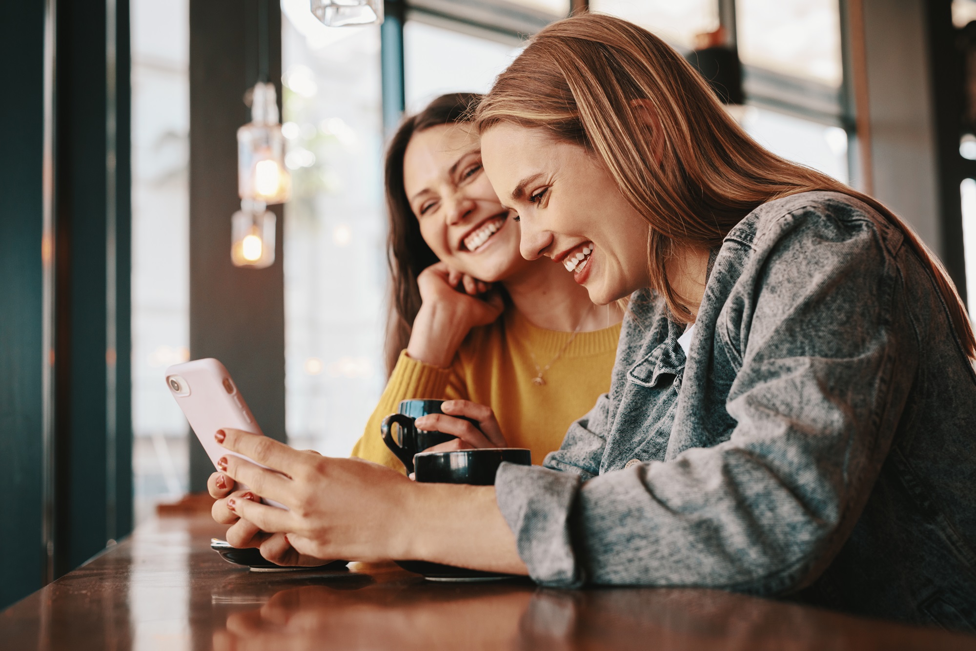 Two female friends smiling and looking at a mobile phone.
