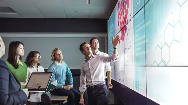 A man presenting on a screen and people looking at what he is presenting