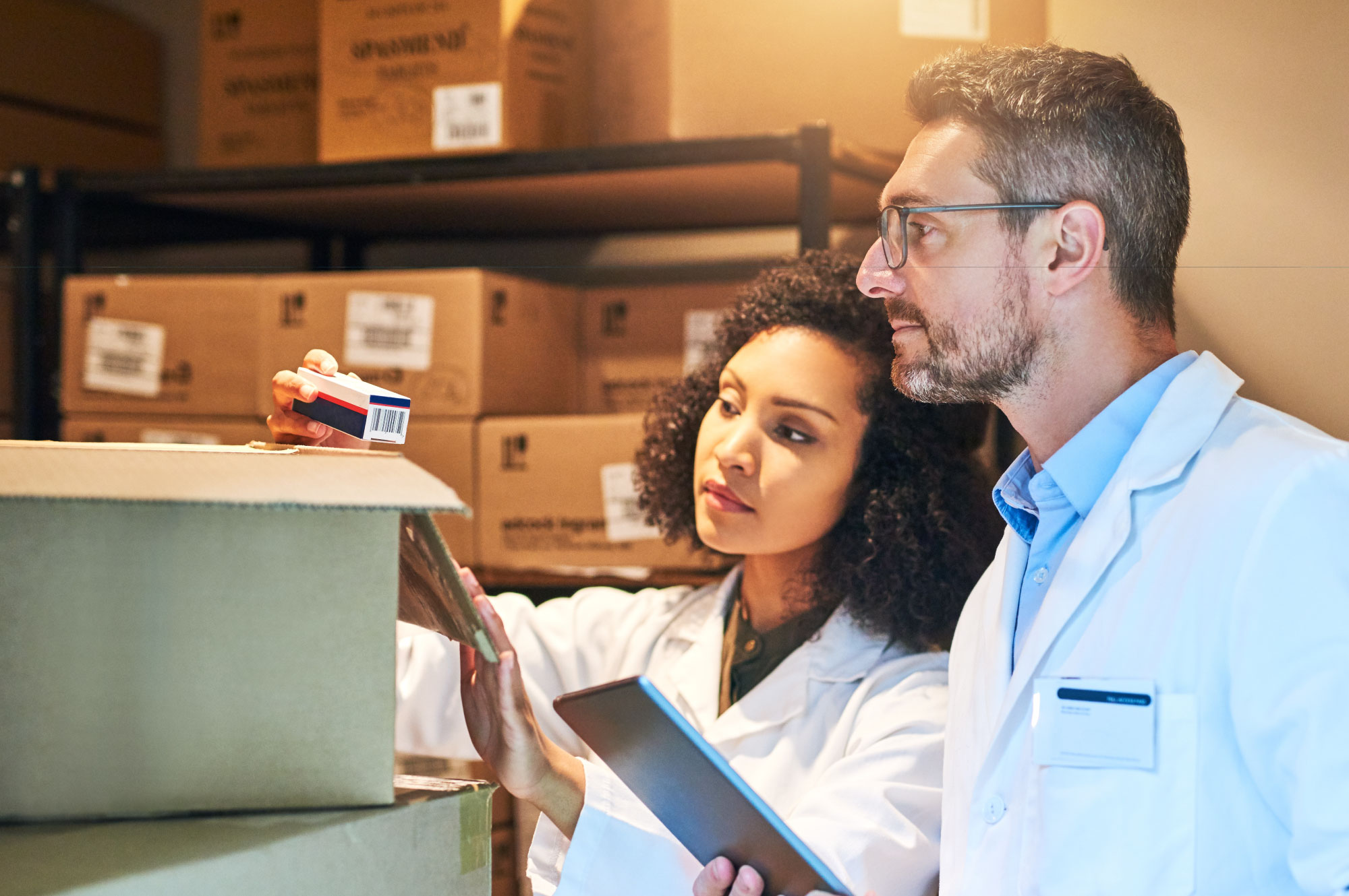 Man and woman in a packaging room wearing medical clothing.