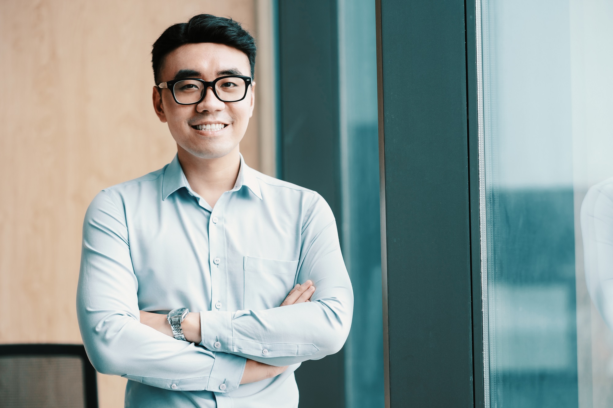 Man standing with his arms crossed smiling in a office.