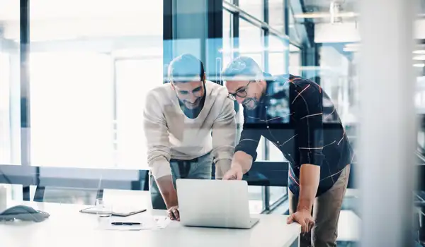 Two man standing up looking interested at a screen