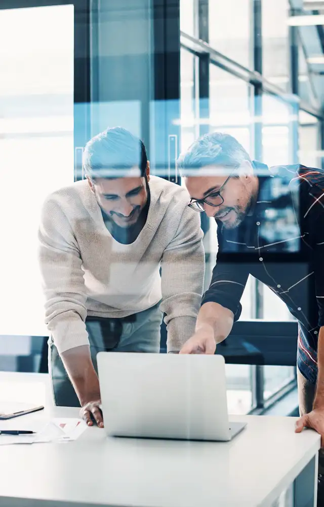 Two man standing up looking interested at a screen