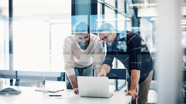 Two man standing up looking interested at a screen
