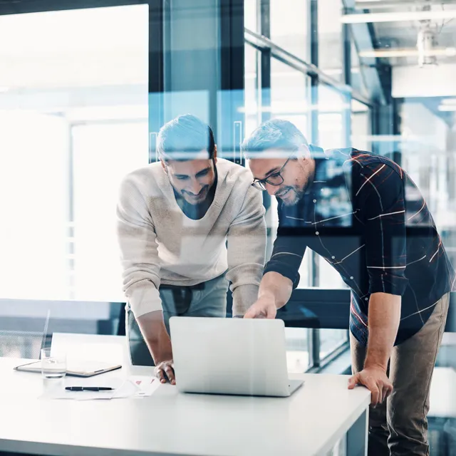 Two man standing up looking interested at a screen