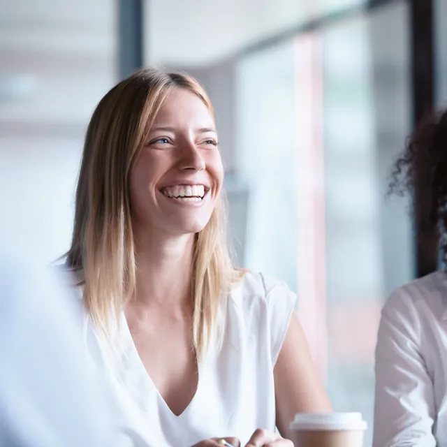 Woman with coffee laughing sitting in business environment