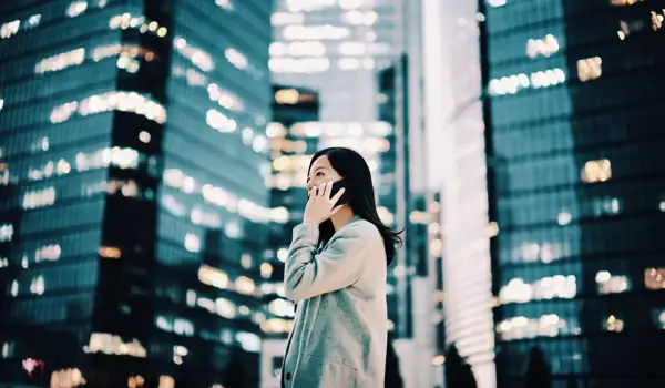 Business woman using her phone standing next to skyscrapers in a city