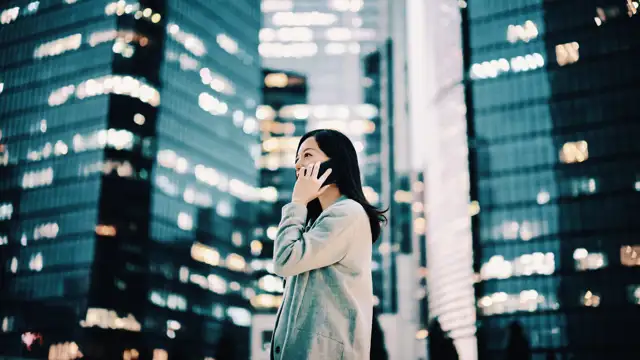 Business woman using her phone standing next to skyscrapers in a city