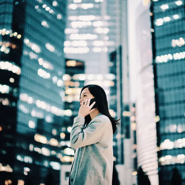 Business woman using her phone standing next to skyscrapers in a city