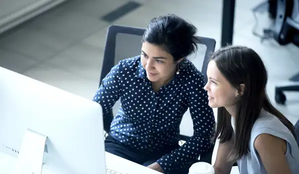 Two happy women looking at a screen and drinking coffee