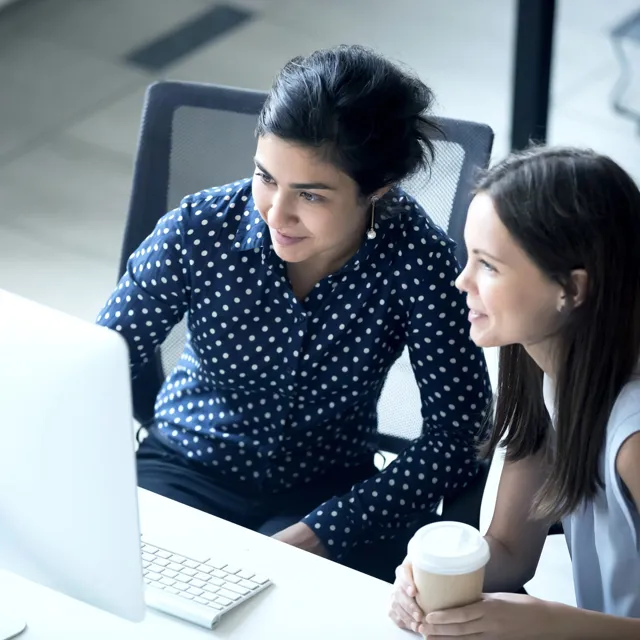Two happy women looking at a screen and drinking coffee